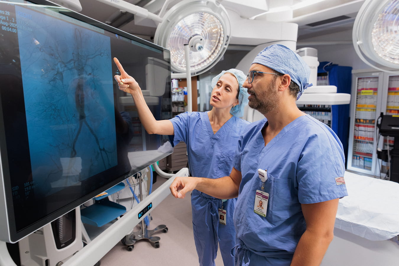 Two HonorHealth medical providers in blue scrubs review a patient scan on a large digital monitor in an advanced clinical setting.