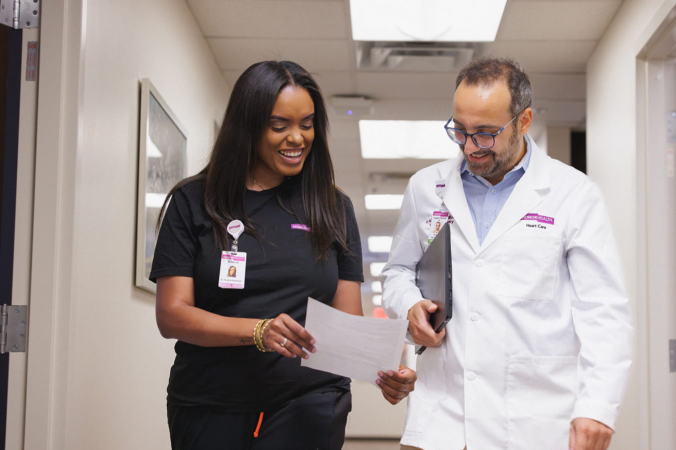 An HonorHealth doctor and a clinical staff member smile and collaborate while walking down a hallway reviewing documents.