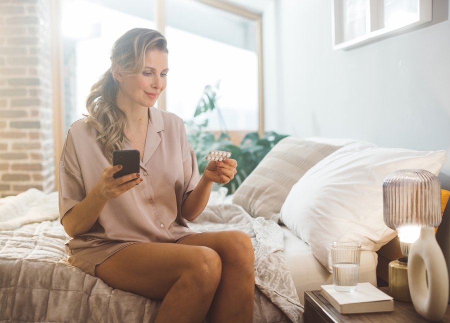 Woman sits in bed looking at hormone replacement therapy (HRT) treatment pills obtained through an HonorHealth OB/GYN.