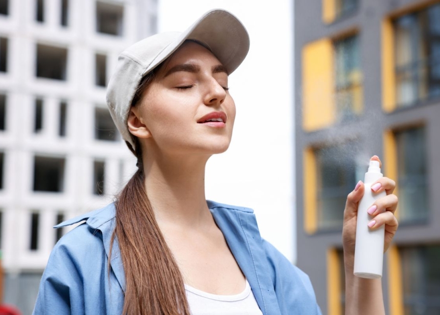 HonorHealth Dermatology - Woman sprays sunscreen on face before going to a Spring Training baseball game.