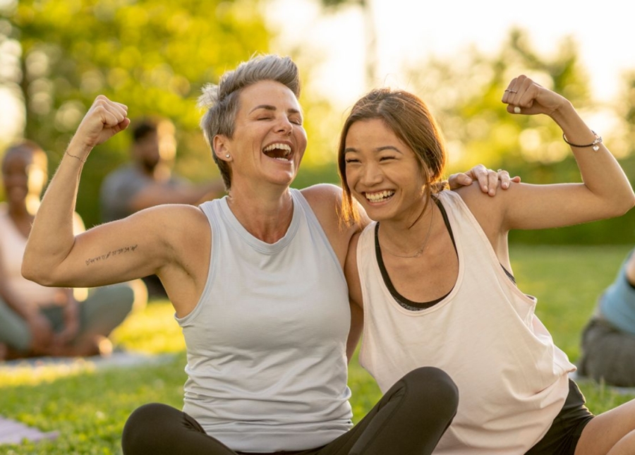 HonorHealth Whole Health Institute - Two smiling women sit in park flexing arm muscles.