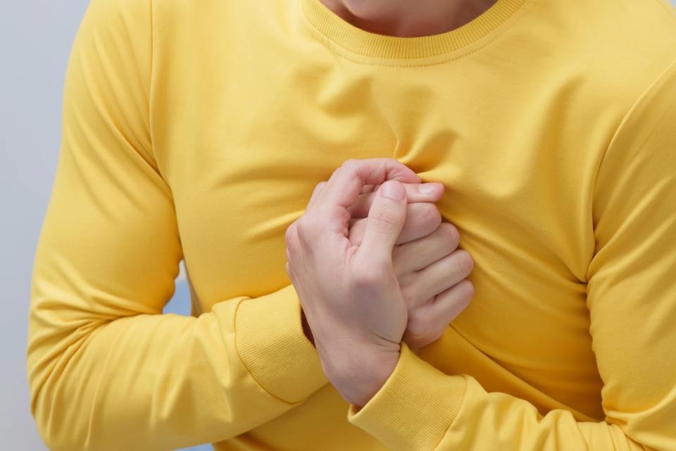 Person in a yellow shirt clutching their chest in apparent pain or distress, illustrating symptoms of broken heart syndrome (Takotsubo cardiomyopathy), a stress-induced heart condition.