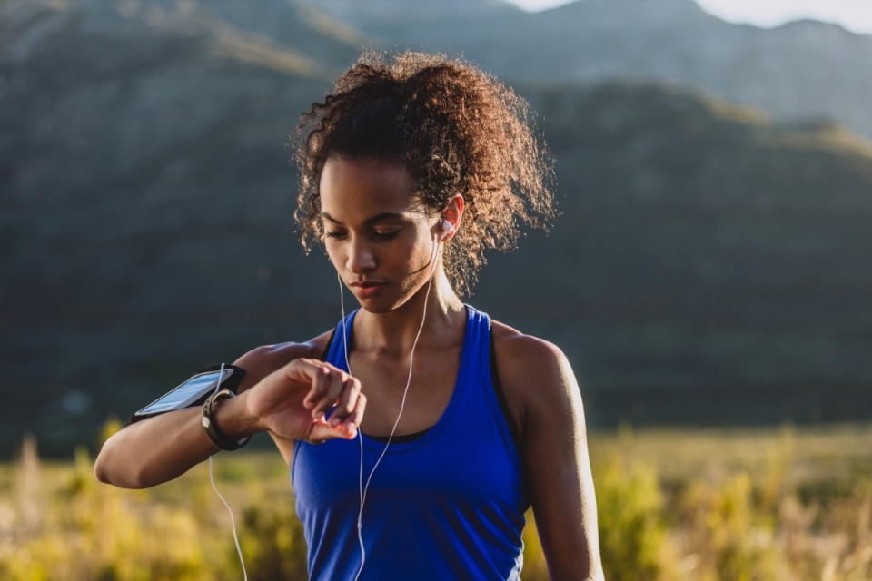 HonorHealth Heart Care - Woman in field looks at smart watch mid-walk trying to reach 10,000 steps.