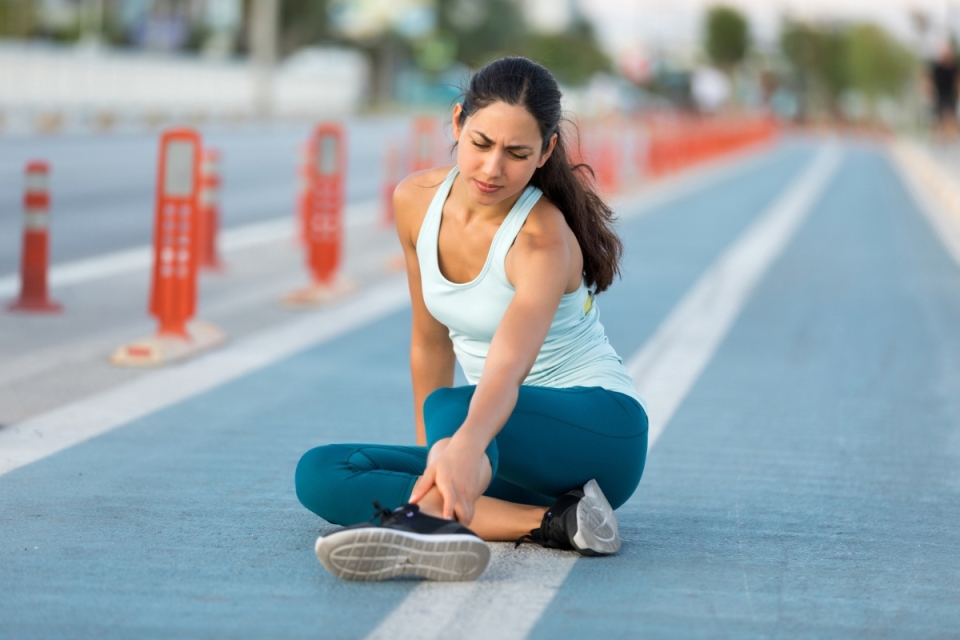 Marathon runner sits down on running track holding ankle injury - HonorHealth Sports Medicine