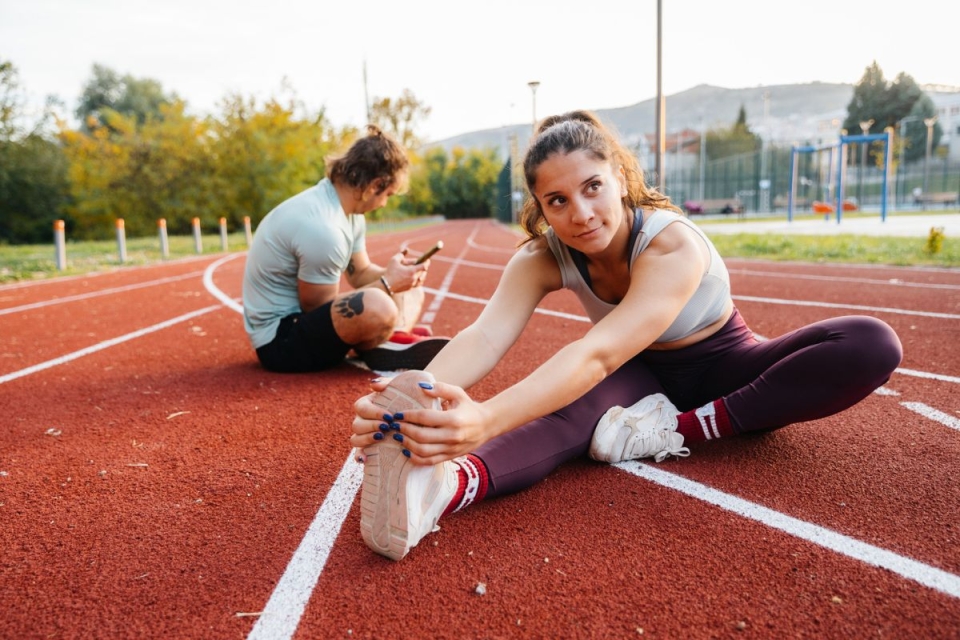 Male and female runners sit on running track and stretch after marathon training - HonorHealth Sports Medicine