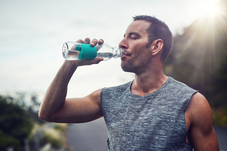 Man takes drink from water bottle outside mid-run - HonorHealth Sports Medicine