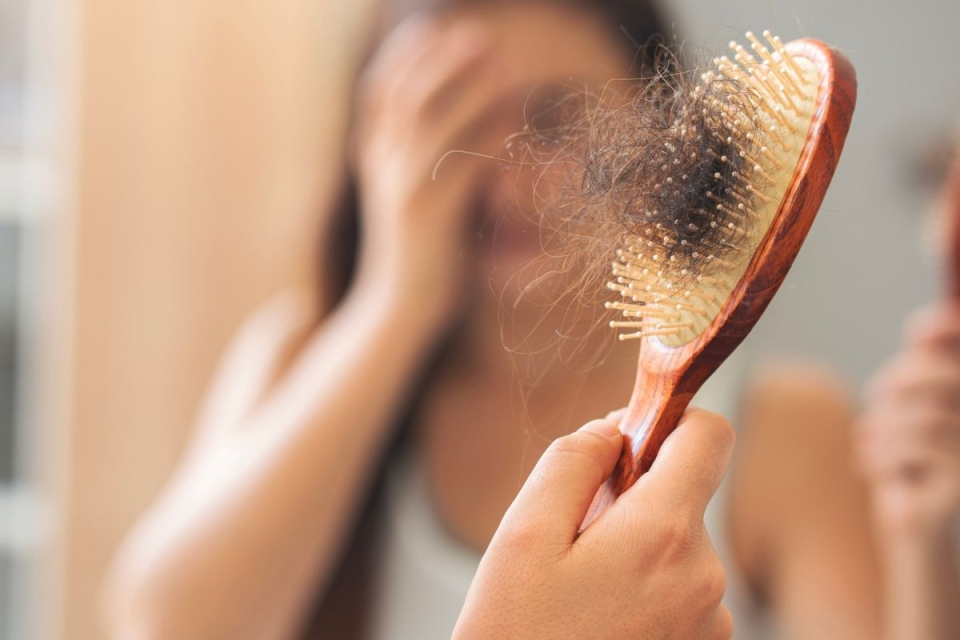 Woman pulls hair out of brush after experiencing menopause hair loss.