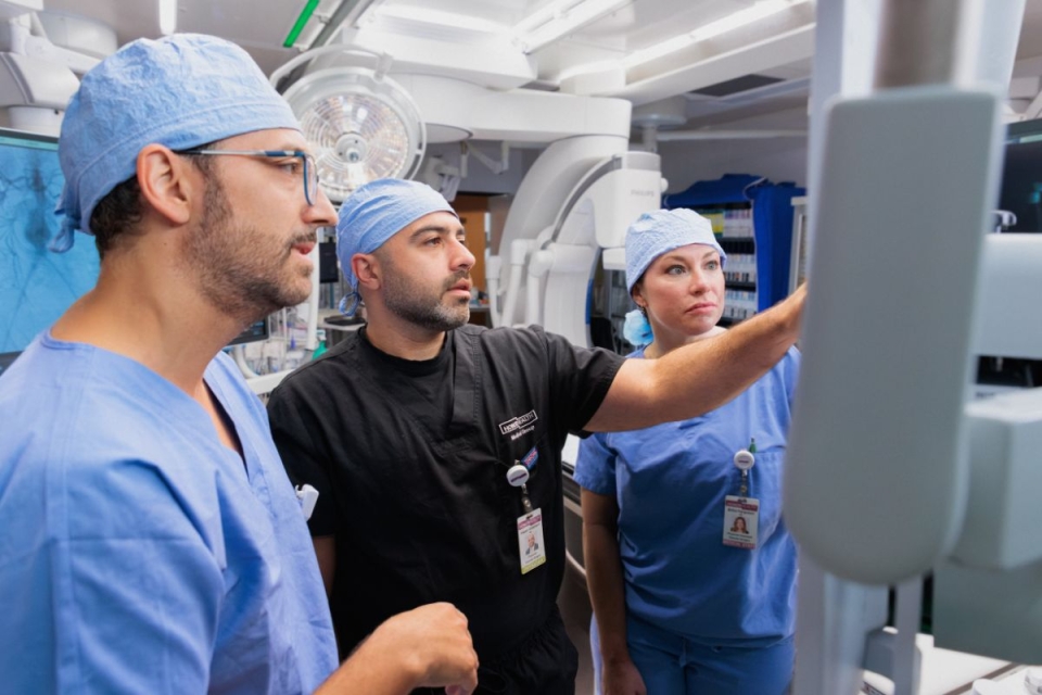 Three HonorHealth Heart Care clinicians in surgical attire reviewing vascular imaging together.