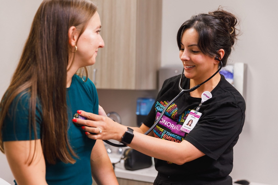 HonorHealth Heart Care - An HonorHealth medical assistant smiling as she places a stethoscope on a patient's chest during an exam.