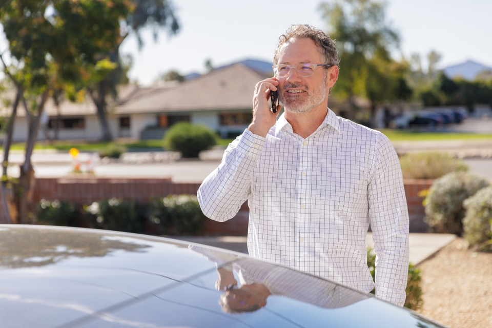 HonorHealth Occupational Medicine - A professional man in a button-down shirt and glasses smiles  outdoors while talking on his mobile phone about supporting employees.