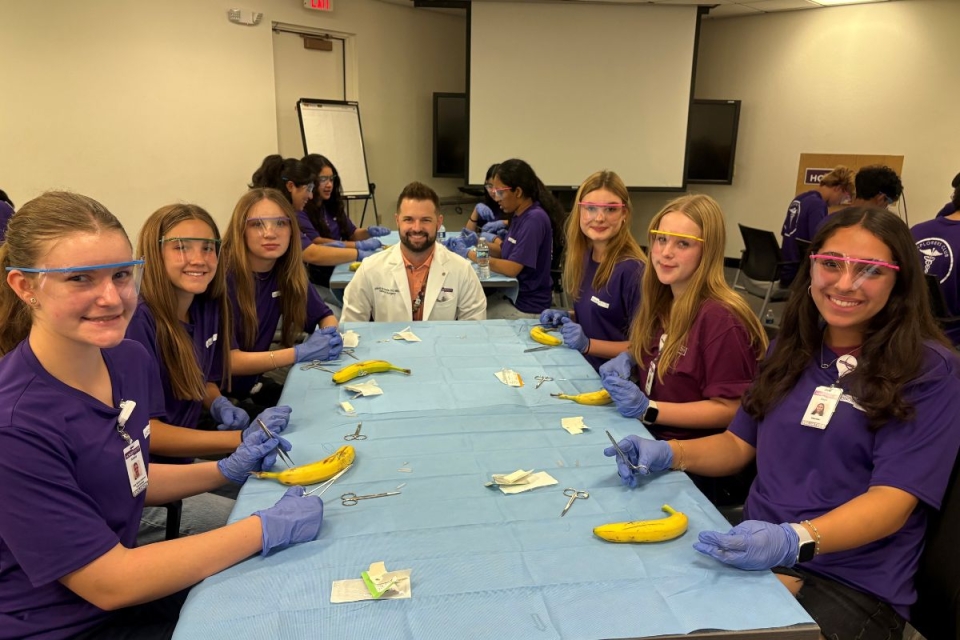 HonorHealth Explorers Club - Group of teen volunteers smile at activity table after learning how to use sutures on bananas with an emergency department physician assistant.