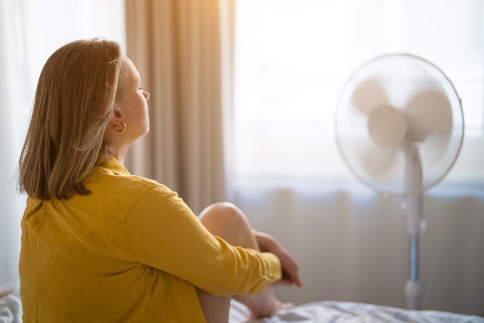 HonorHealth Primary Care - Woman sits in front of fan sitting on bed after a sleepless night due to summer heat.