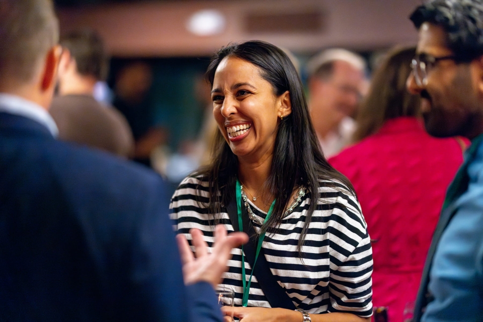 A woman in a striped shirt laughs during a conversation at a medical staff social.
