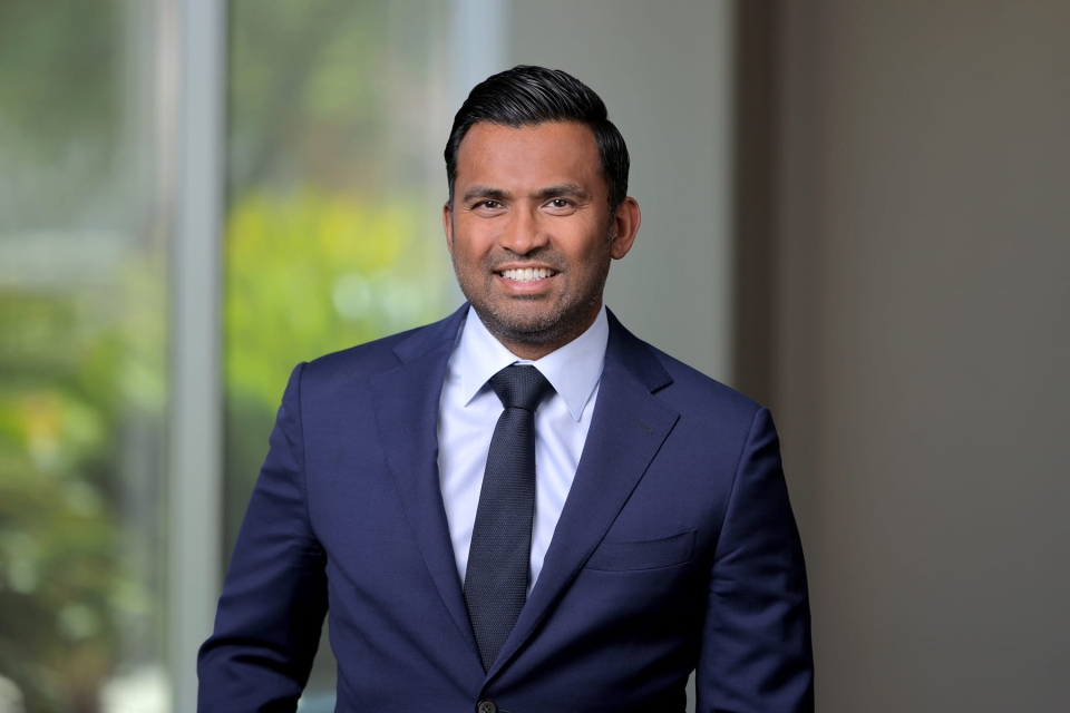 Professional headshot of Dr. Ajit Itty smiling in a navy blue suit jacket, light blue dress shirt and dark tie.