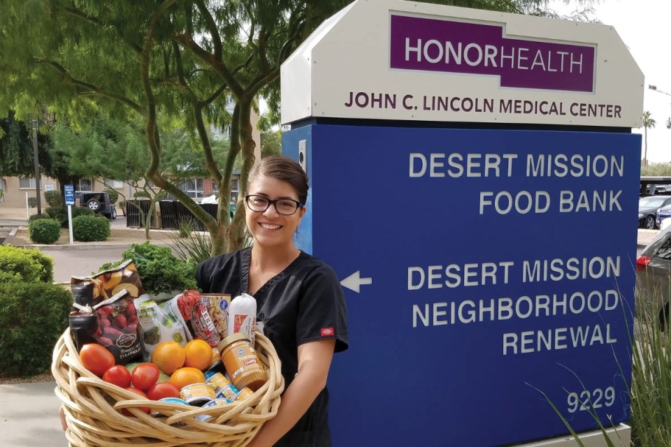 HonorHealth Desert Mission Food Bank volunteer smiles while holding donation basket of produce.