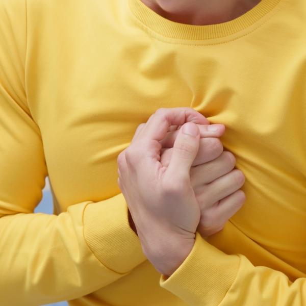 Person in a yellow shirt clutching their chest in apparent pain or distress, illustrating symptoms of broken heart syndrome (Takotsubo cardiomyopathy), a stress-induced heart condition.