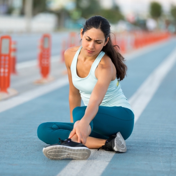Marathon runner sits down on running track holding ankle injury - HonorHealth Sports Medicine
