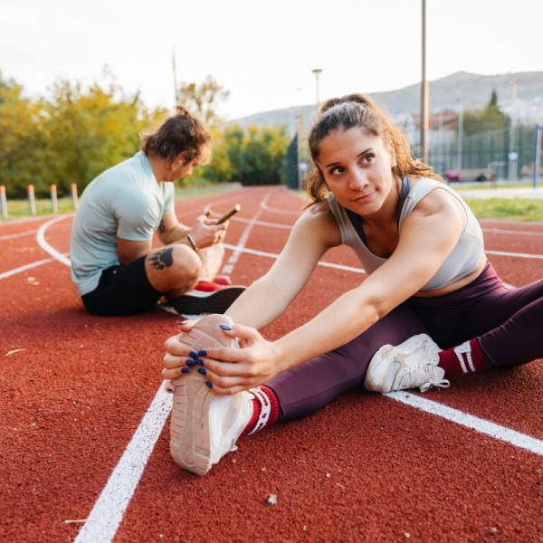Male and female runners sit on running track and stretch after marathon training - HonorHealth Sports Medicine