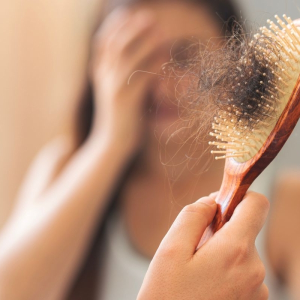 Woman pulls hair out of brush after experiencing menopause hair loss.