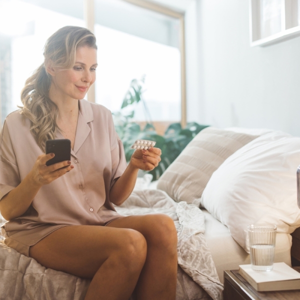 Woman sits in bed looking at hormone replacement therapy (HRT) treatment pills obtained through an HonorHealth OB/GYN.