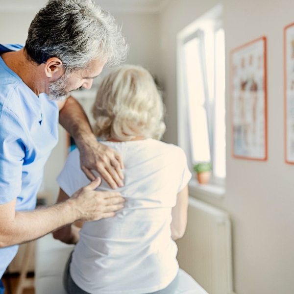 HonorHealth physician uses hands-on manual therapy to address upper back pain in an older patient, illustrating fascial distortion treatment by peeling back tissue layers to relieve stubborn pain.