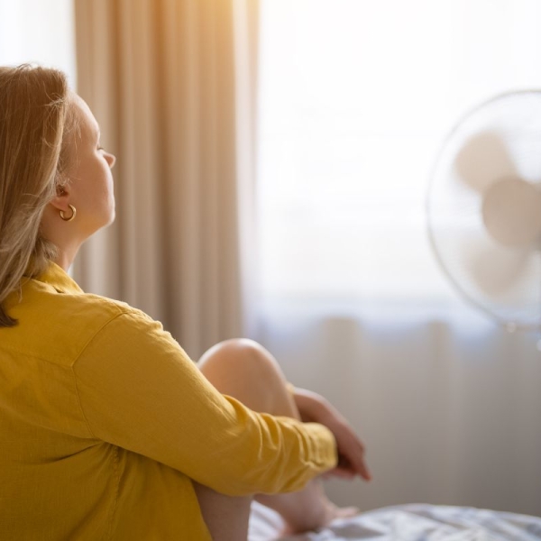 HonorHealth Primary Care - Woman sits in front of fan sitting on bed after a sleepless night due to summer heat.