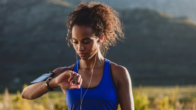 HonorHealth Heart Care - Woman in field looks at smart watch mid-walk trying to reach 10,000 steps.