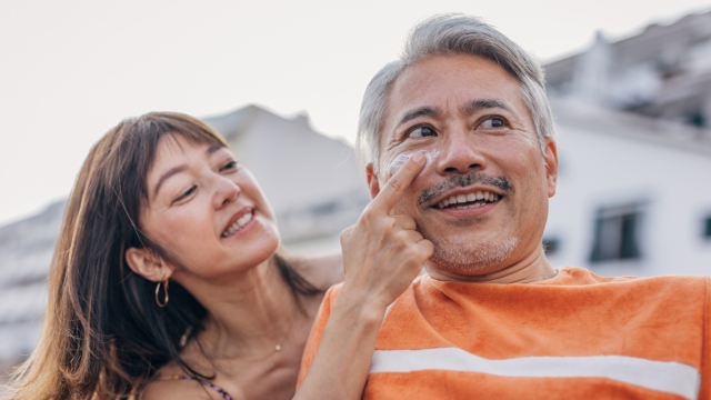 HonorHealth Dermatology - Woman rubs sunscreen onto man's face to prevent skin cancer.