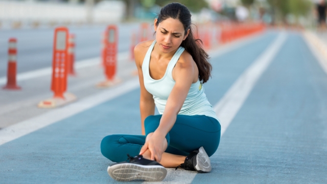 Marathon runner sits down on running track holding ankle injury - HonorHealth Sports Medicine