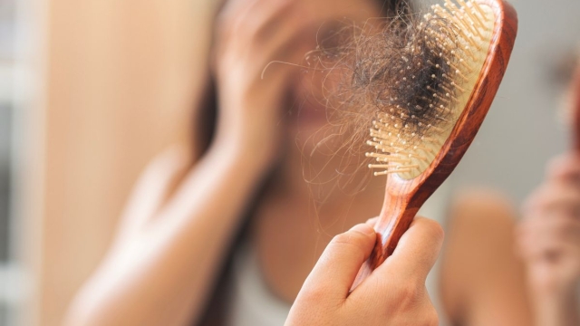 Woman pulls hair out of brush after experiencing menopause hair loss.