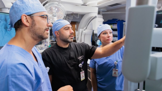 Three HonorHealth Heart Care clinicians in surgical attire reviewing vascular imaging together.