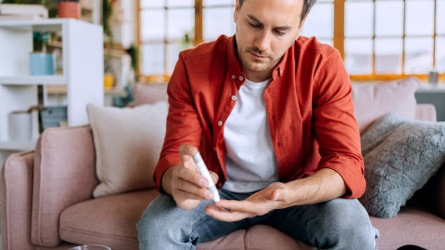 HonorHealth diabetes management - Male patient sits on couch and pricks finger as a part of his HonorHealth diabetes management plan.