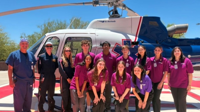 Students in HonorHealth's High School Volunteer Program stand with instructor in front of emergency medical helicopter.