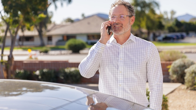 HonorHealth Occupational Medicine - A professional man in a button-down shirt and glasses smiles  outdoors while talking on his mobile phone about supporting employees.