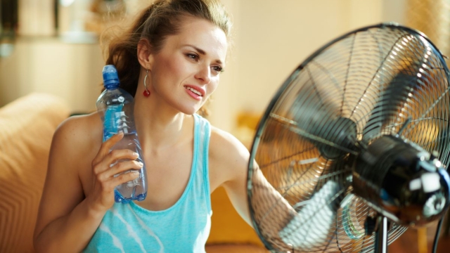 HonorHealth Medical Group - Woman sits in front of fan and holds cold water bottle on neck to cool down during summer heat.