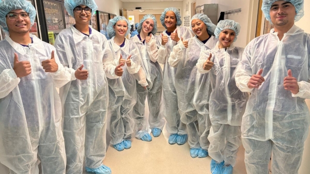 HonorHealth Explorers Club - Group of teen volunteers dressed in operating scrubs smile with thumbs up in group photo.
