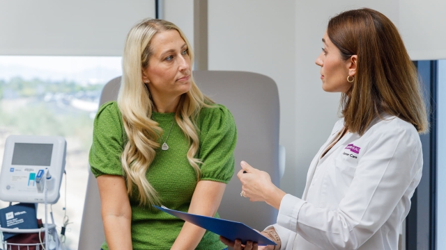 A physician wearing an HonorHealth Cancer Care lab coat speaks with a patient during a consultation in an exam room.